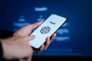 Pessoa segura celular com logo da OpenAI e ChatGPT na tela.