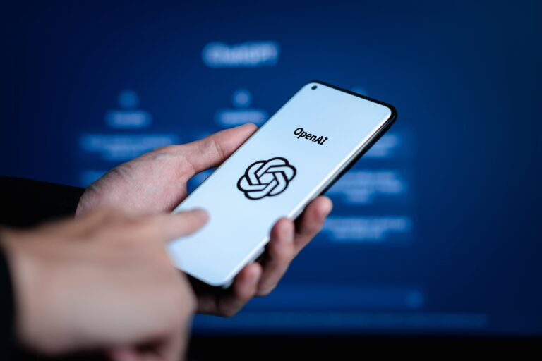 Pessoa segura celular com logo da OpenAI e ChatGPT na tela.