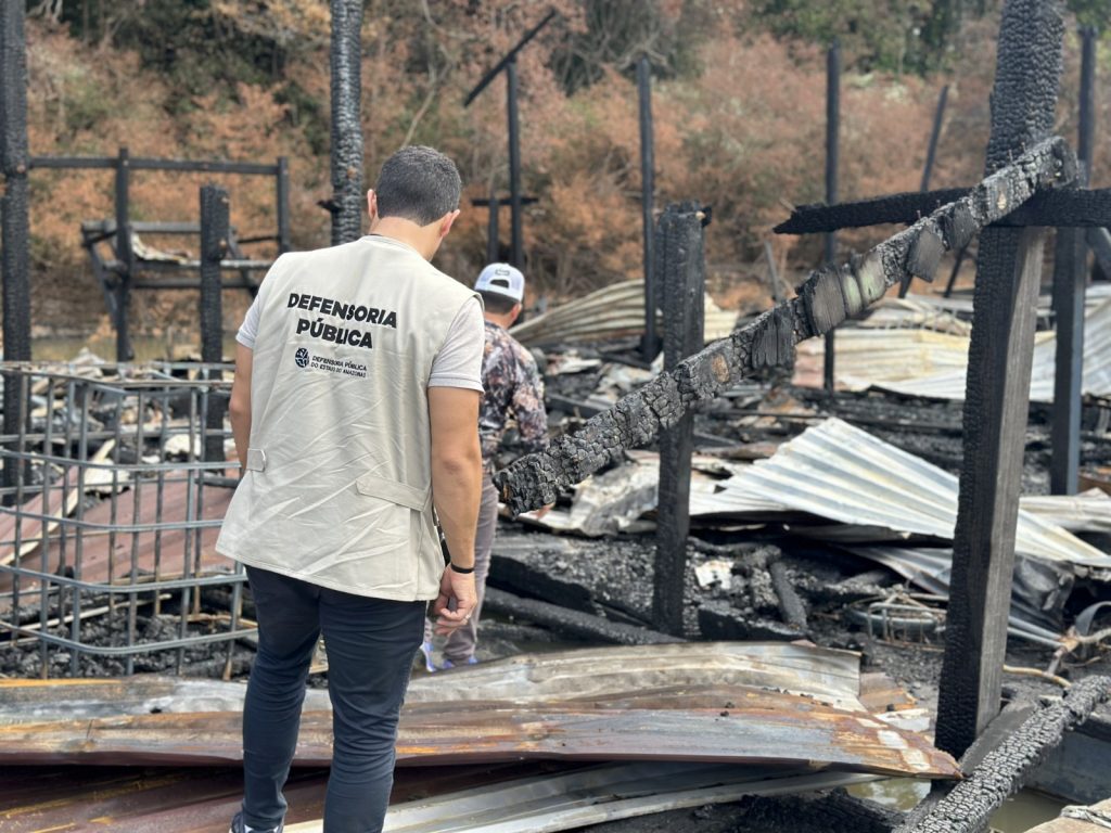Agente da Defensoria Pública do Amazonas caminha entre destroços queimados de balsas em Humaitá após operação contra garimpo no rio Madeira