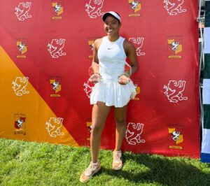 Jovem tenista amazonense, vestindo roupa branca de competição, segura dois troféus após vitória no Torneio ITF 60 em Concepción, Chile.