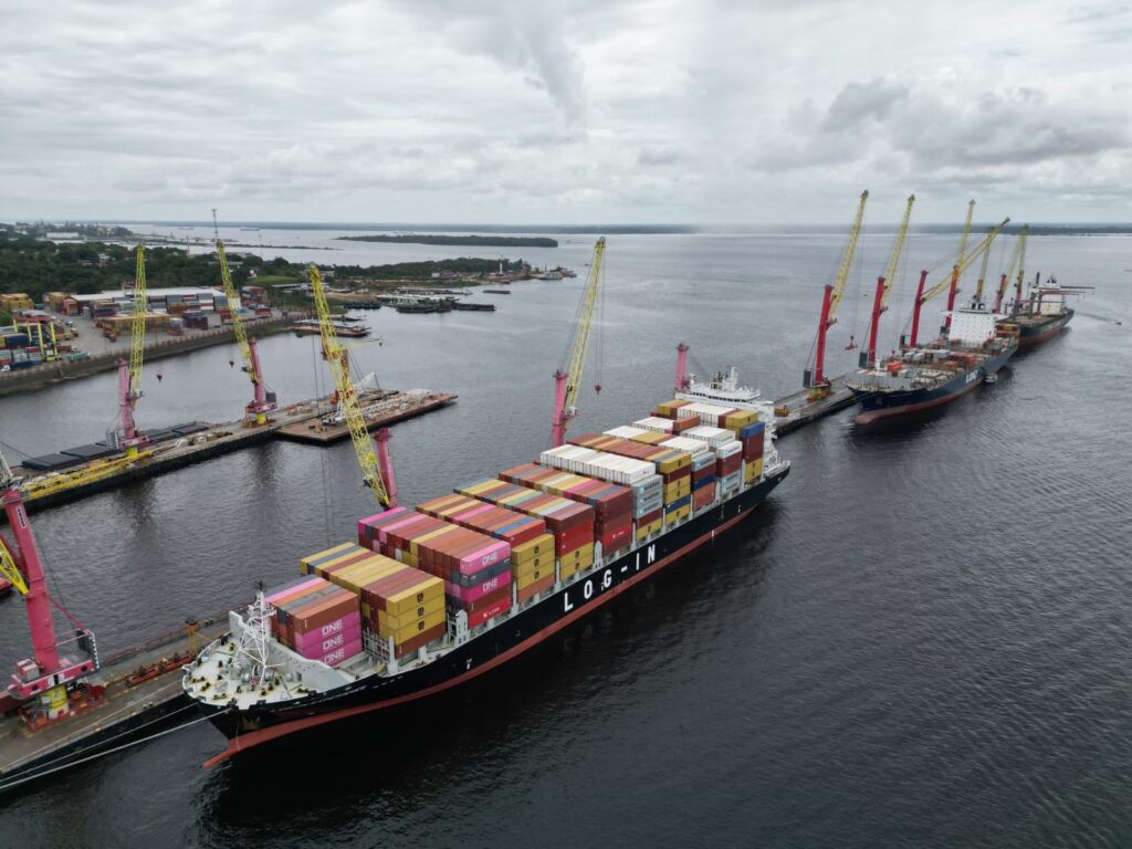 Navio com contêineres atracado no Porto de Manaus durante operação de carga e descarga, com guindastes em funcionamento.