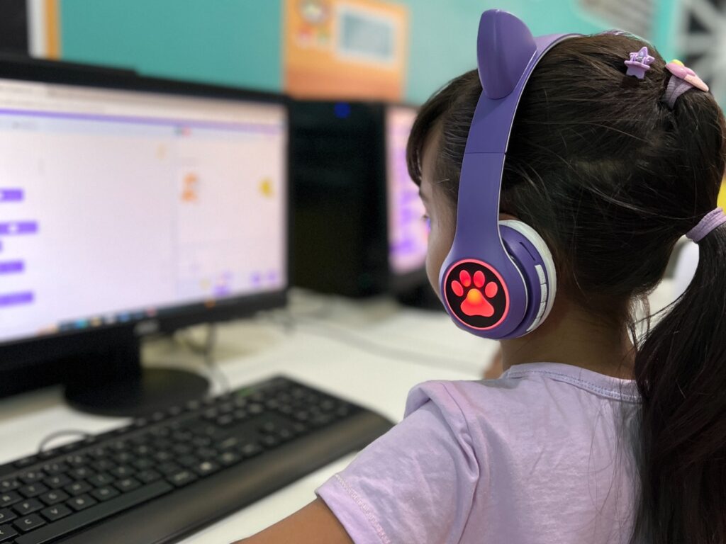 Menina com fones de ouvido roxos usa computador durante aula de programação no projeto Manaós Tech Girls.