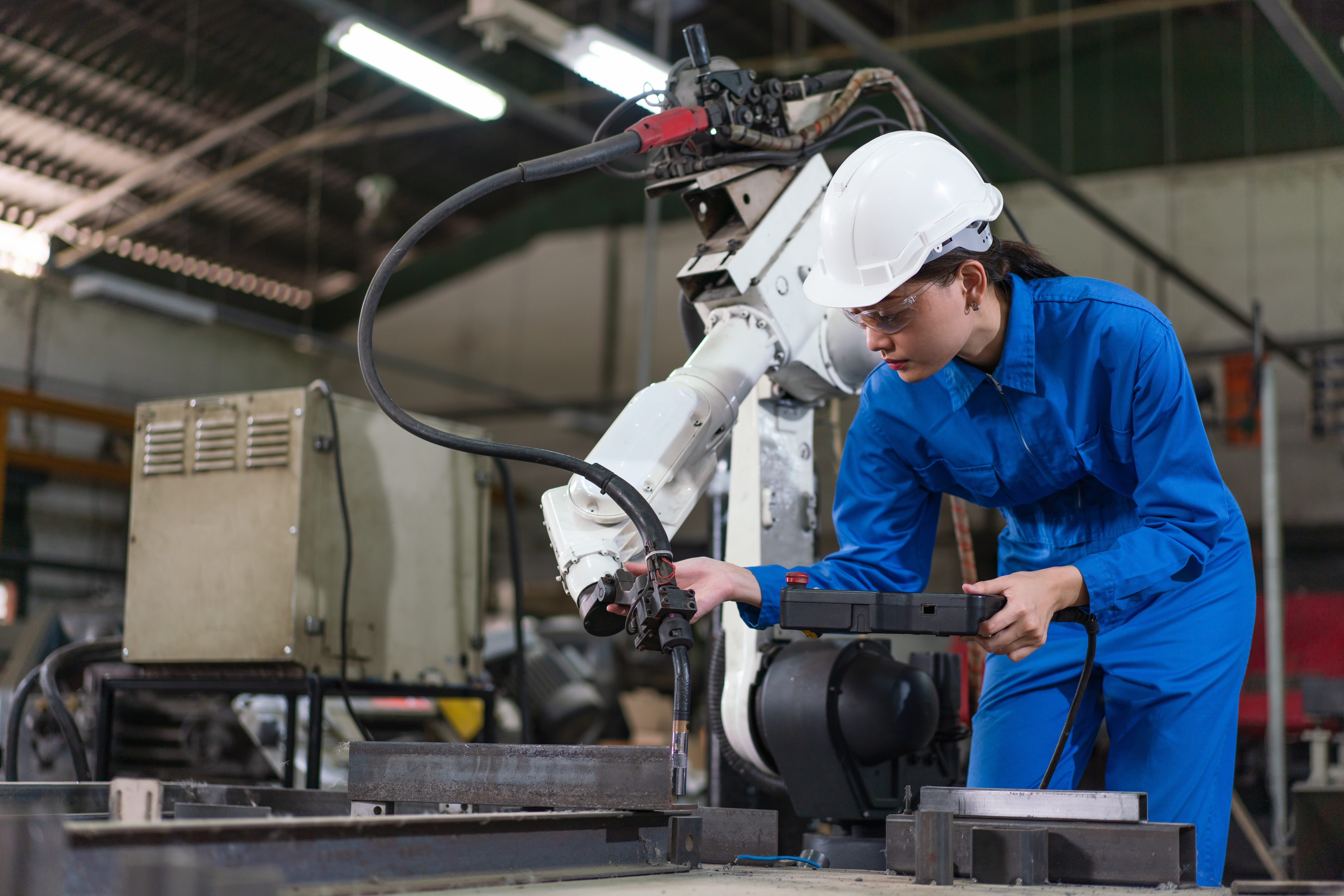 Trabalhadora opera sistema automatizado com apoio de robô industrial em fábrica brasileira.
