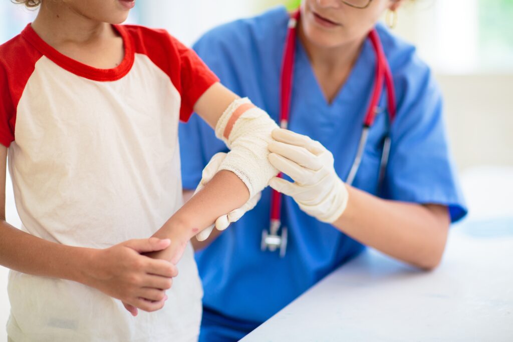 Médica atende criança com braço enfaixado após acidente doméstico.