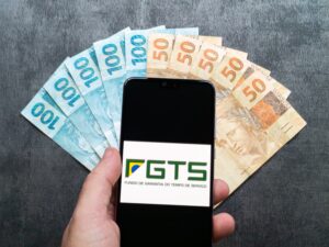 Celular com logotipo do FGTS à frente de notas de real brasileiras