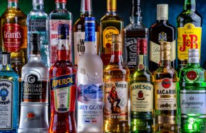 Várias garrafas de bebidas alcoólicas de diferentes marcas e cores organizadas lado a lado em prateleira.