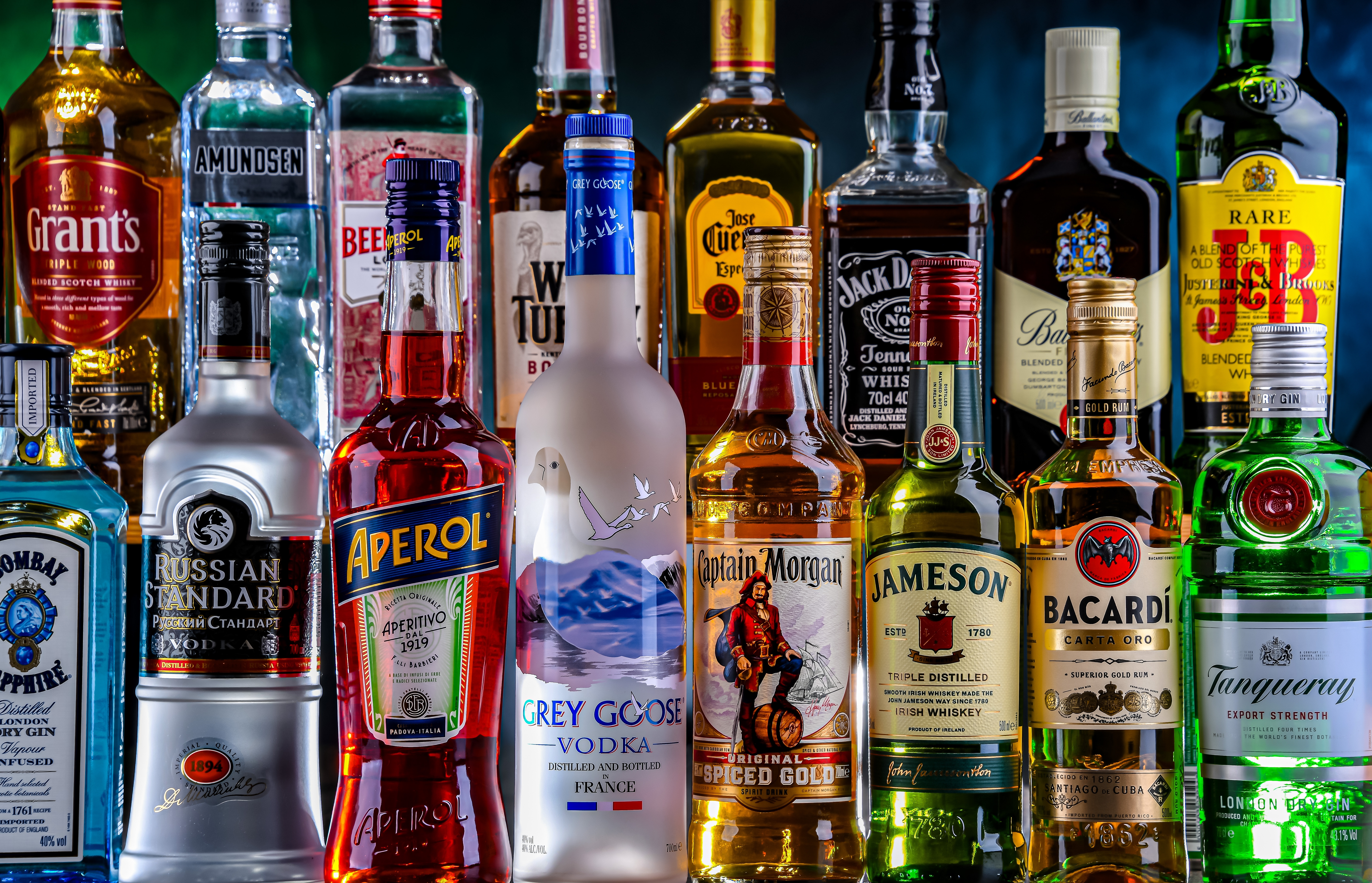 Várias garrafas de bebidas alcoólicas de diferentes marcas e cores organizadas lado a lado em prateleira.