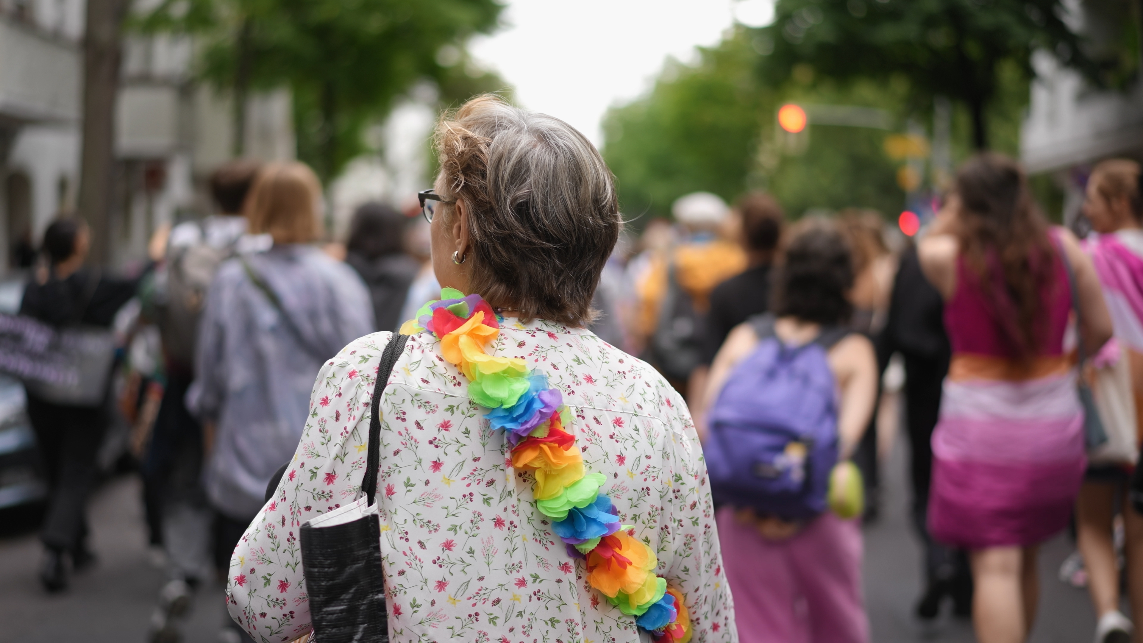 Mulher com colar de flores coloridas caminha em meio a multidão durante evento de rua.