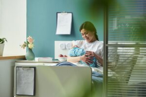 Mulher deitada em leito hospitalar sorri enquanto segura seu bebê recém-nascido enrolado em manta azul.