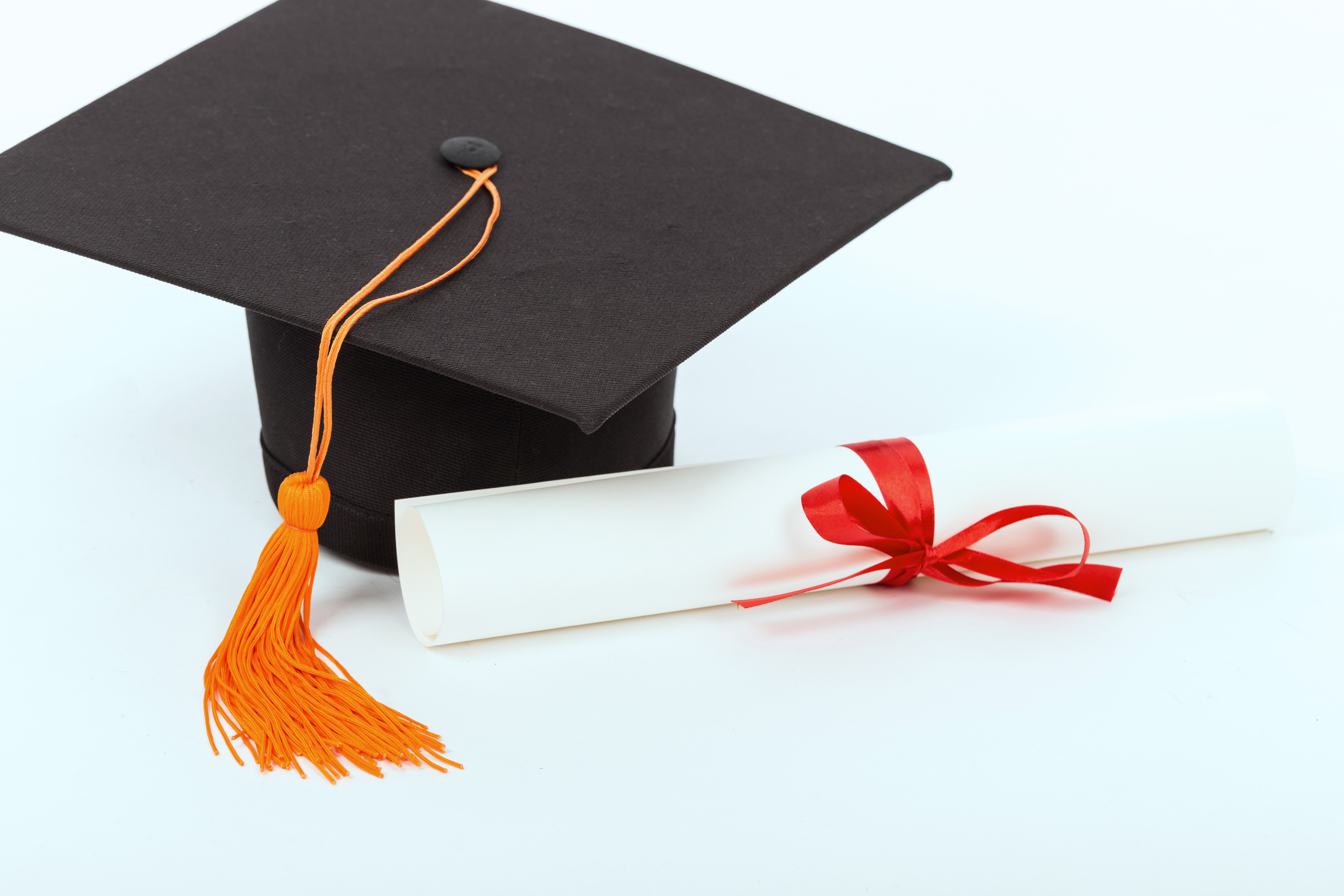 Chapéu de formatura com tassel laranja ao lado de diploma enrolado com laço vermelho.