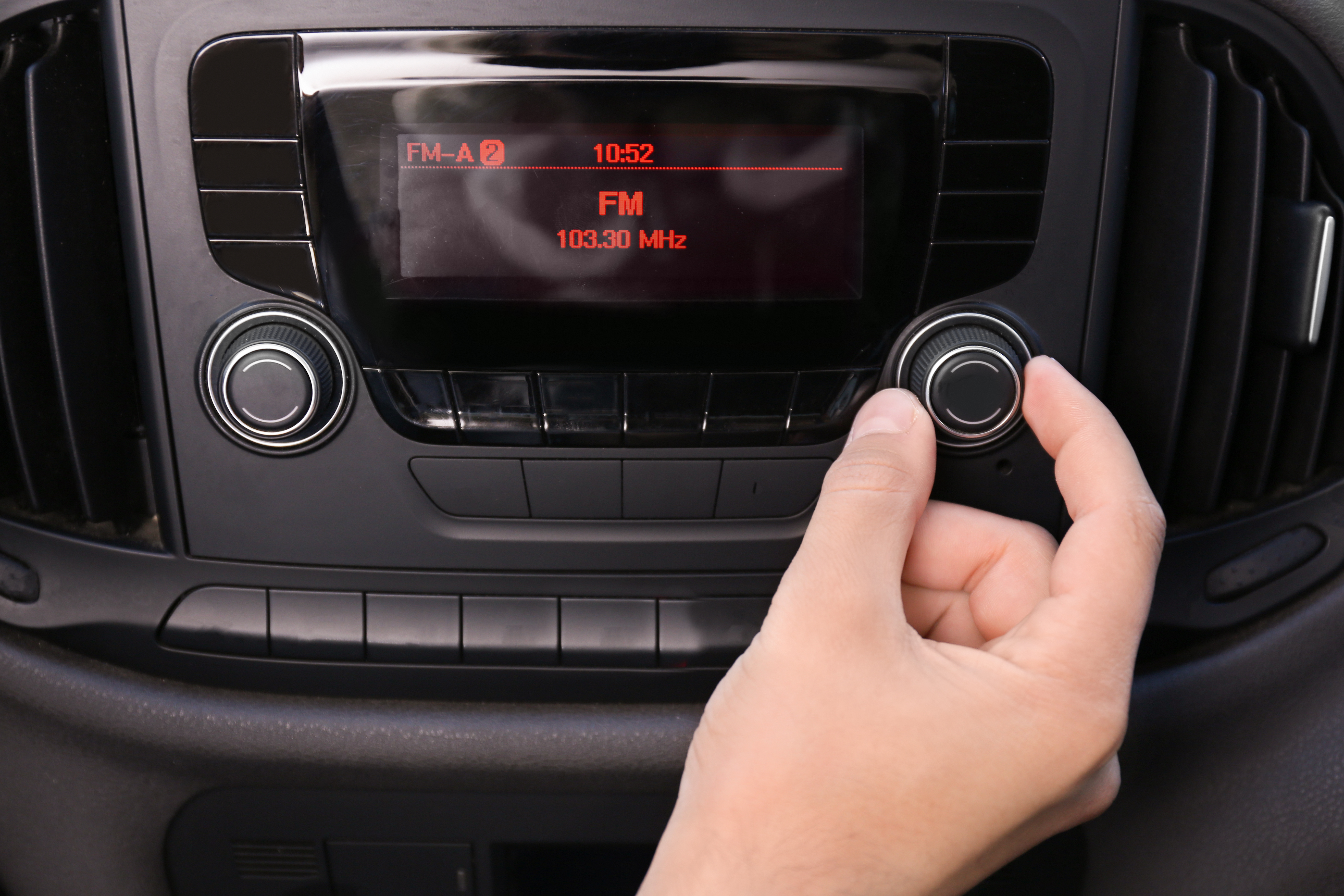 Mão ajustando o dial de rádio no carro, símbolo da resistência do meio na era digital