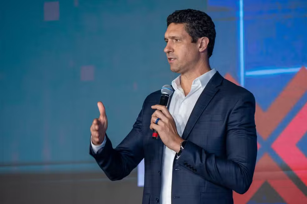 Ex-nadador Gustavo Borges fala em evento, usando microfone e terno azul, durante palestra.