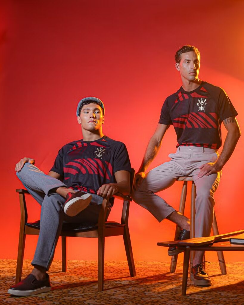 Nova camisa do Flamengo em homenagem aos 130 anos, exibida sobre fundo vermelho, traz escudo dourado e padronagem inspirada nas ondas da Baía de Guanabara.
