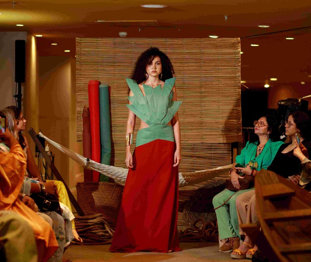 Modelo desfila vestido em cores verde e vermelho inspirado na natureza amazônica durante o Amazon Poranga Fashion, em Manaus, com público acompanhando ao redor da passarela.