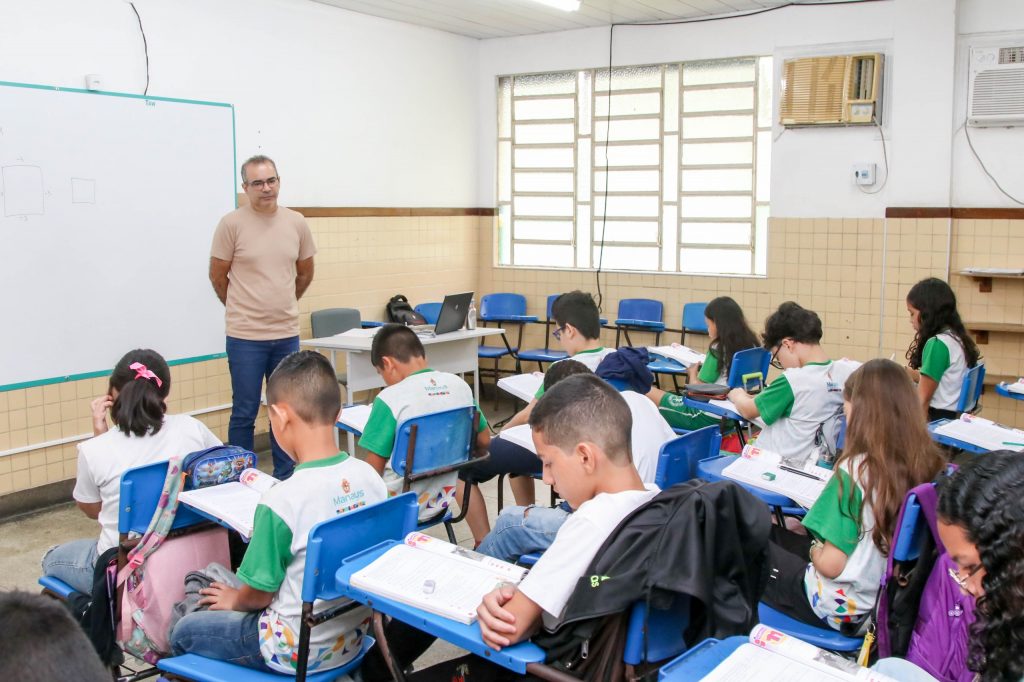 Professor em sala de aula com alunos da rede municipal de Manaus durante atividade escolar.