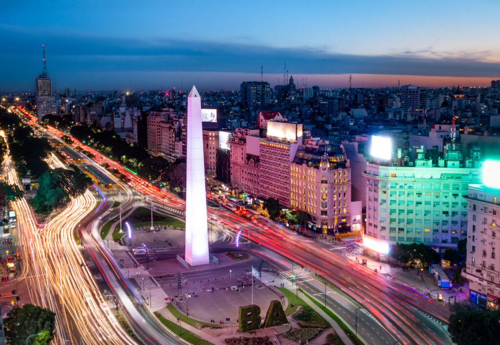 Vista aérea do Obelisco de Buenos Aires à noite, com luzes e tráfego intenso nas avenidas