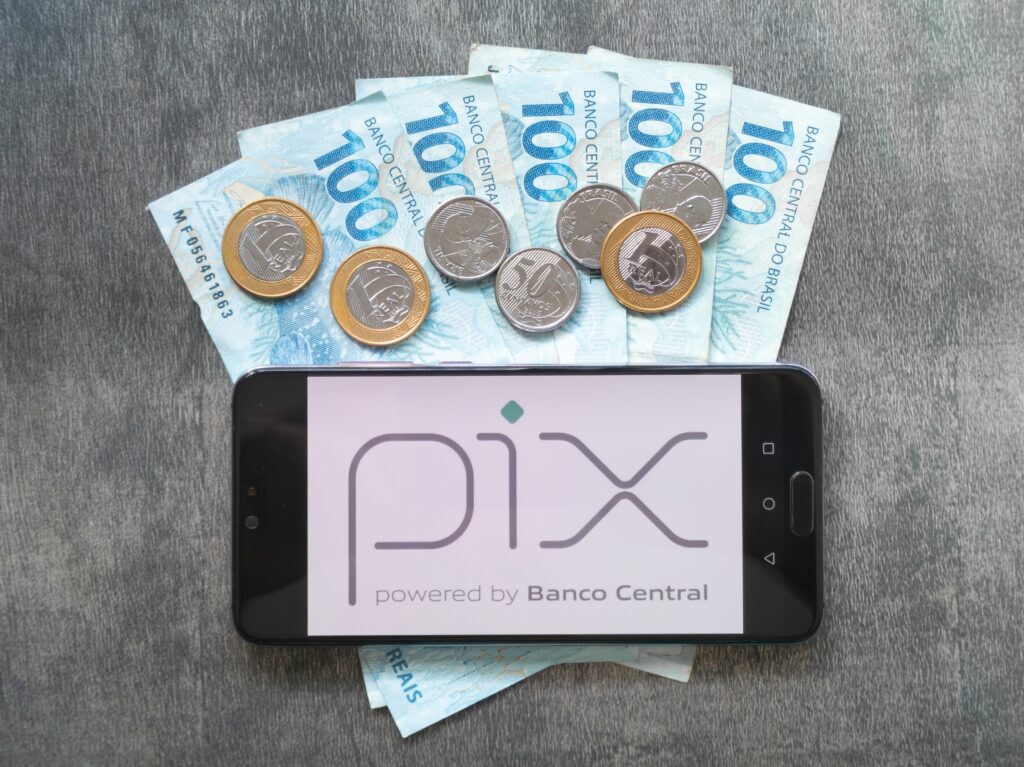 Celular com logo do Pix sobre notas e moedas brasileiras, simbolizando novo botão de contestação para fraudes.