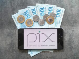 Celular com logo do Pix sobre notas e moedas brasileiras, simbolizando novo botão de contestação para fraudes.