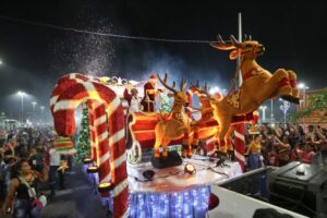 Carro alegórico natalino com rena e trenó desfilando durante a Parada Natalina em Manaus