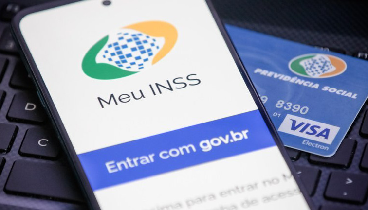 Tela do aplicativo Meu INSS em smartphone sobre teclado, ao lado de cartão de benefício da Previdência Social.