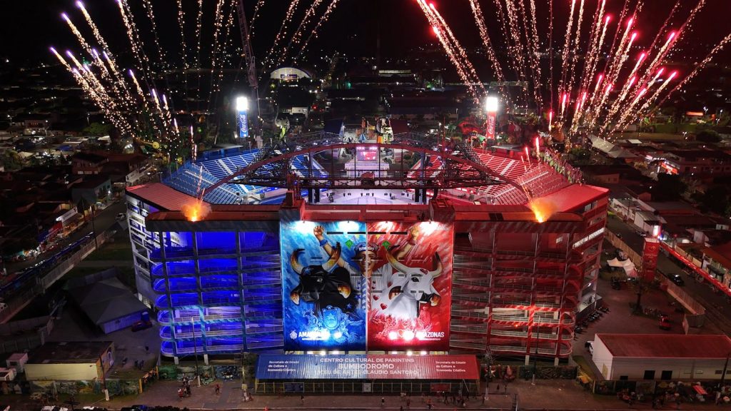 Vista aérea do Bumbódromo durante o Festival de Parintins com fogos e arquibancadas azul e vermelha
