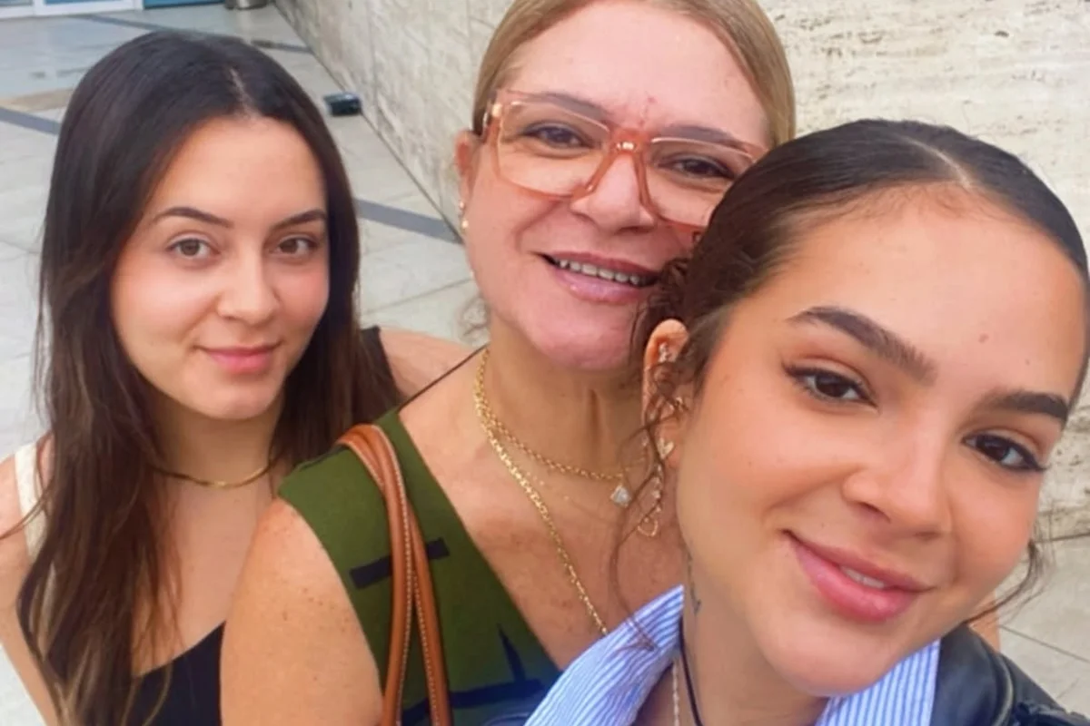 Mel Maia ao lado da mãe, Débora Maia, e de outra familiar em foto sorrindo tirada ao ar livre.