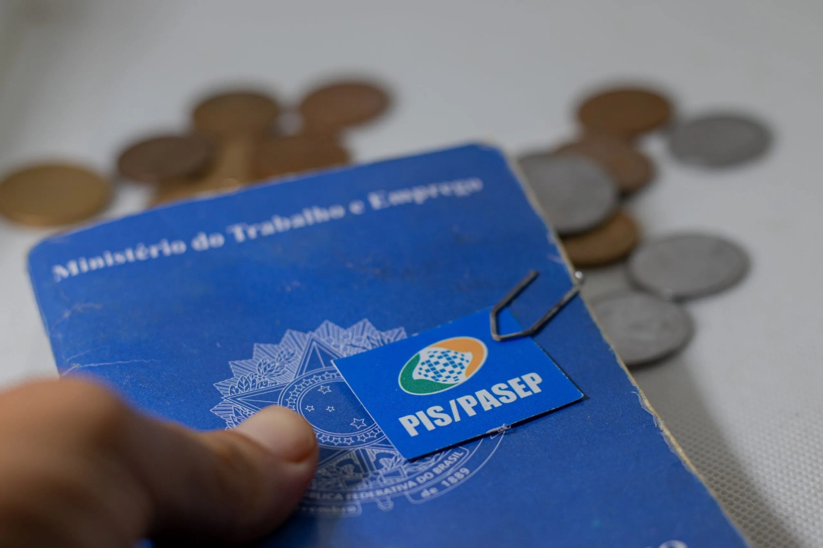 Carteira de Trabalho com etiqueta do PIS/Pasep sobre mesa com moedas ao fundo