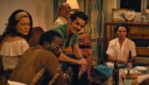 Cena do filme “O Agente Secreto” mostra Wagner Moura e outros atores reunidos em uma sala de estar, em clima descontraído.