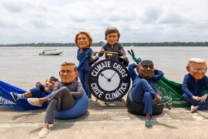 Ativistas caracterizados como líderes mundiais em redes e pufes com relógio escrito “crise climática” em Belém