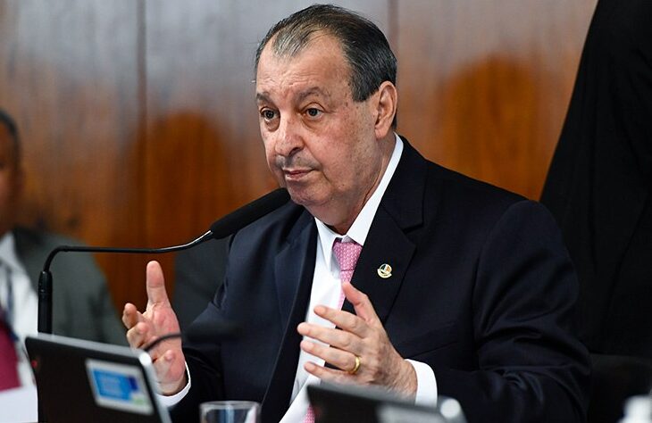 Omar Aziz falando ao microfone durante sessão no Senado, sentado à mesa com documentos e computadores à frente.
