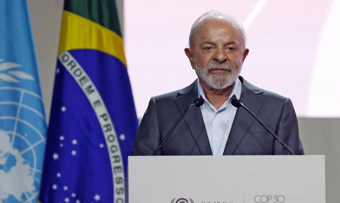 Lula discursando na abertura da COP 30 em Belém, com bandeiras do Brasil e da ONU ao fundo.