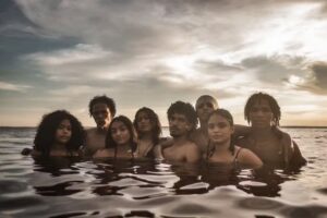 Grupo de jovens negros e negras dentro de um rio na Amazônia, durante o pôr do sol, olhando para a câmera e simbolizando a negritude amazônica.