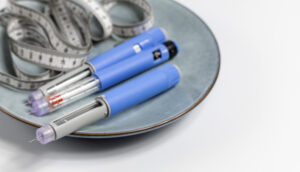 Três canetas injetáveis de medicamentos GLP-1, semelhantes ao Ozempic, colocadas sobre um prato com uma fita métrica, simbolizando tratamentos para obesidade.