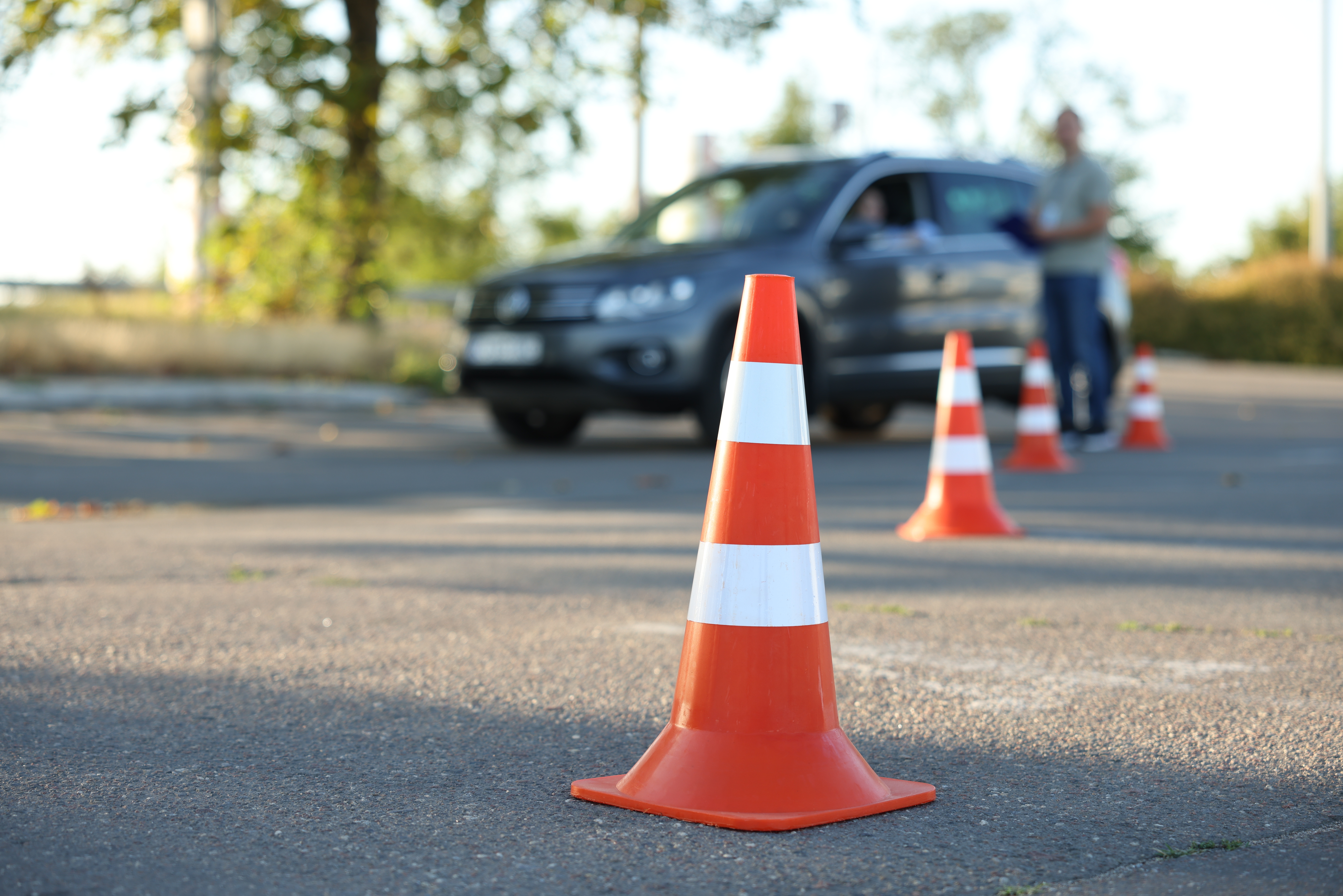 Cone de trânsito em primeiro plano durante exame prático de direção com carro ao fundo.