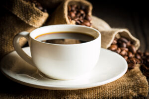 Xícara de café preto ao lado de grãos torrados sobre pano rústico, simbolizando estudo que associa o consumo moderado de café ao envelhecimento celular mais lento.