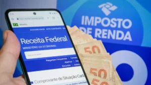 Celular exibindo site da Receita Federal ao lado de dinheiro e símbolo do Imposto de Renda.