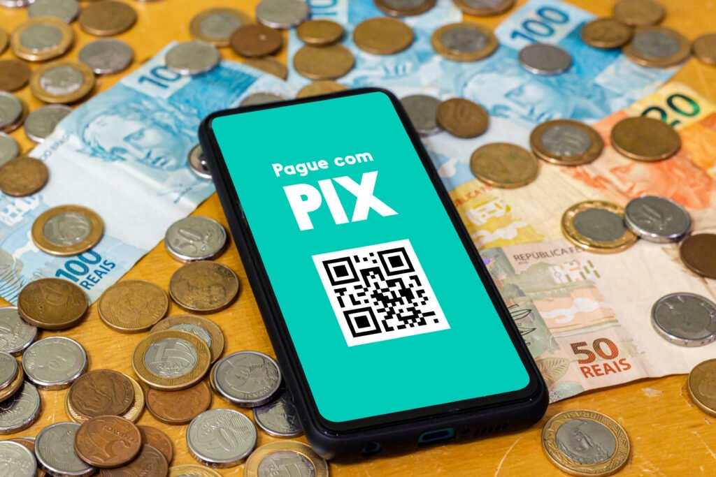 Celular exibe tela de pagamento via Pix sobre notas e moedas de real.