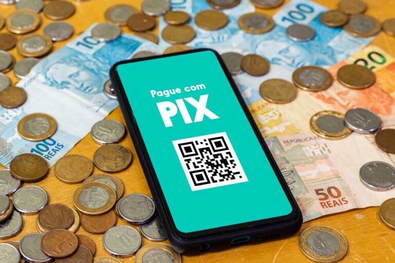 Celular exibe tela de pagamento via Pix sobre notas e moedas de real.