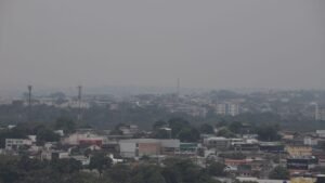 Vista panorâmica de Manaus encoberta pela fumaça, com prédios e árvores sob céu acinzentado