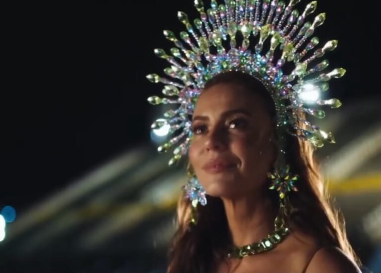 Paolla Oliveira usando uma coroa de pedrarias coloridas e acessórios brilhantes durante apresentação de Carnaval.