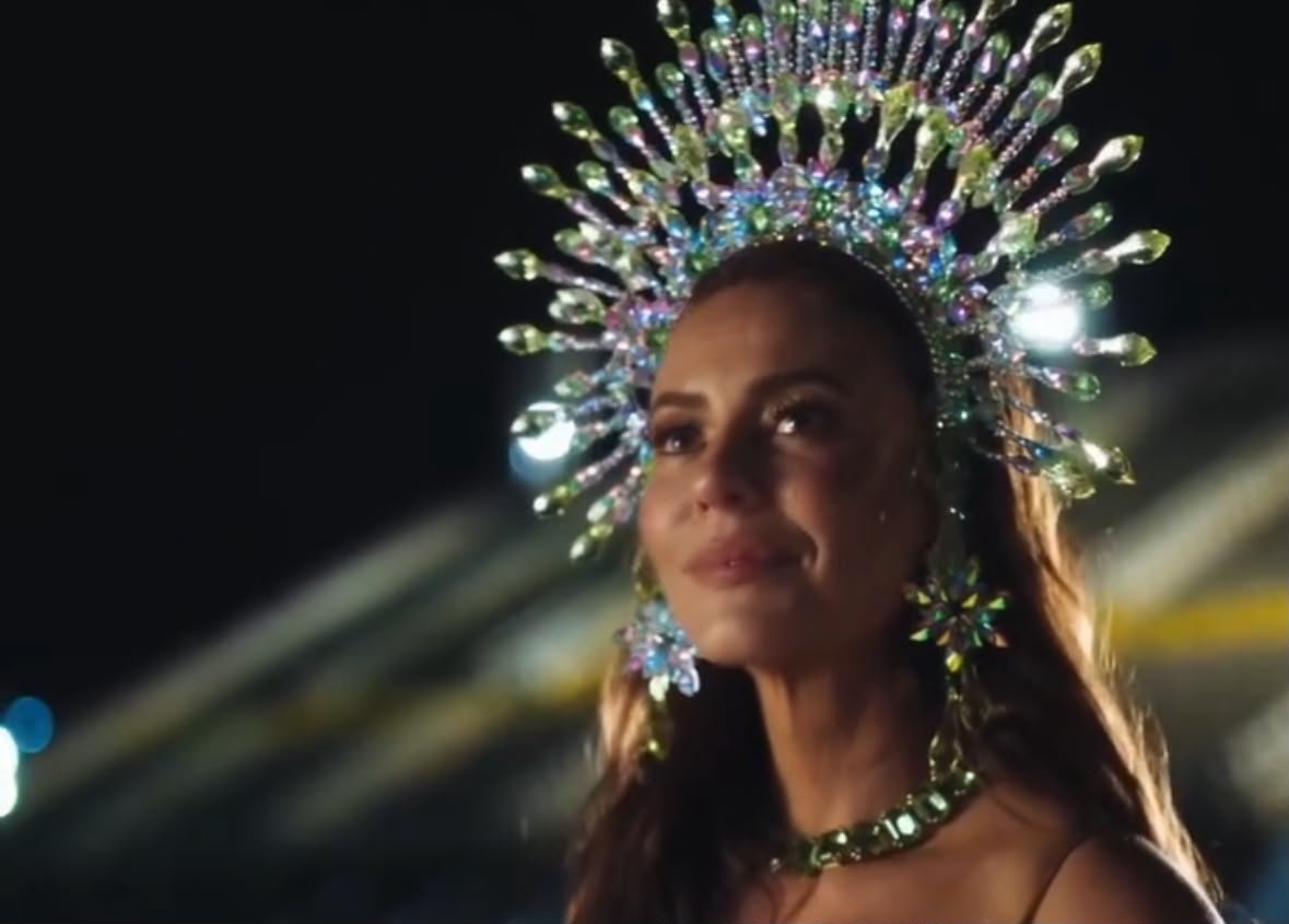 Paolla Oliveira usando uma coroa de pedrarias coloridas e acessórios brilhantes durante apresentação de Carnaval.