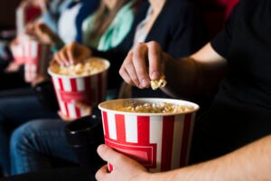 Pessoas assistem a filme com pipoca em sala de cinema