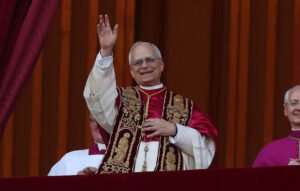 Papa Leão XIV acena de uma sacada, acompanhado por integrantes da Igreja Católica