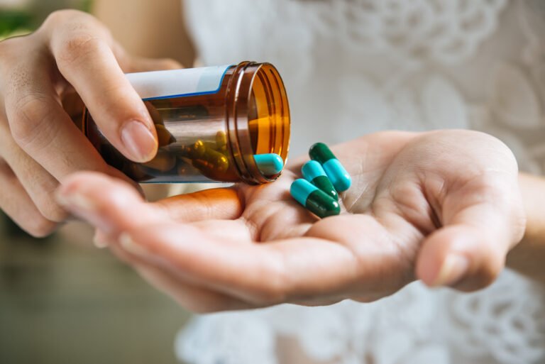 Pessoa segurando frasco de medicamento e cápsulas nas mãos