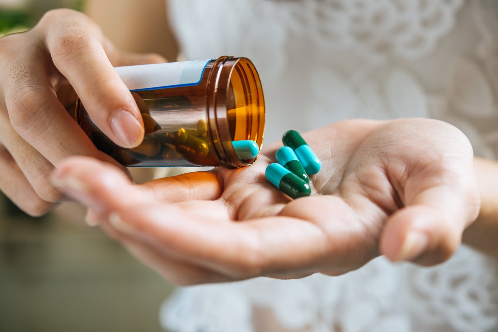Pessoa segurando frasco de medicamento e cápsulas nas mãos