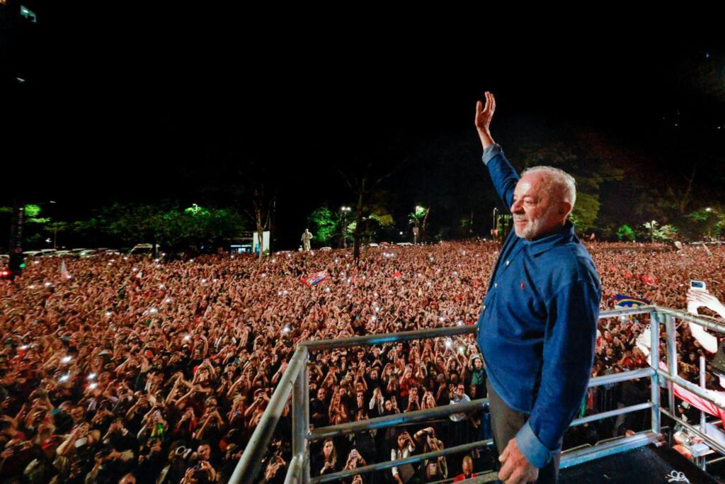 Presidente Luiz Inácio Lula da Silva acena para uma multidão de apoiadores durante evento político realizado à noite.