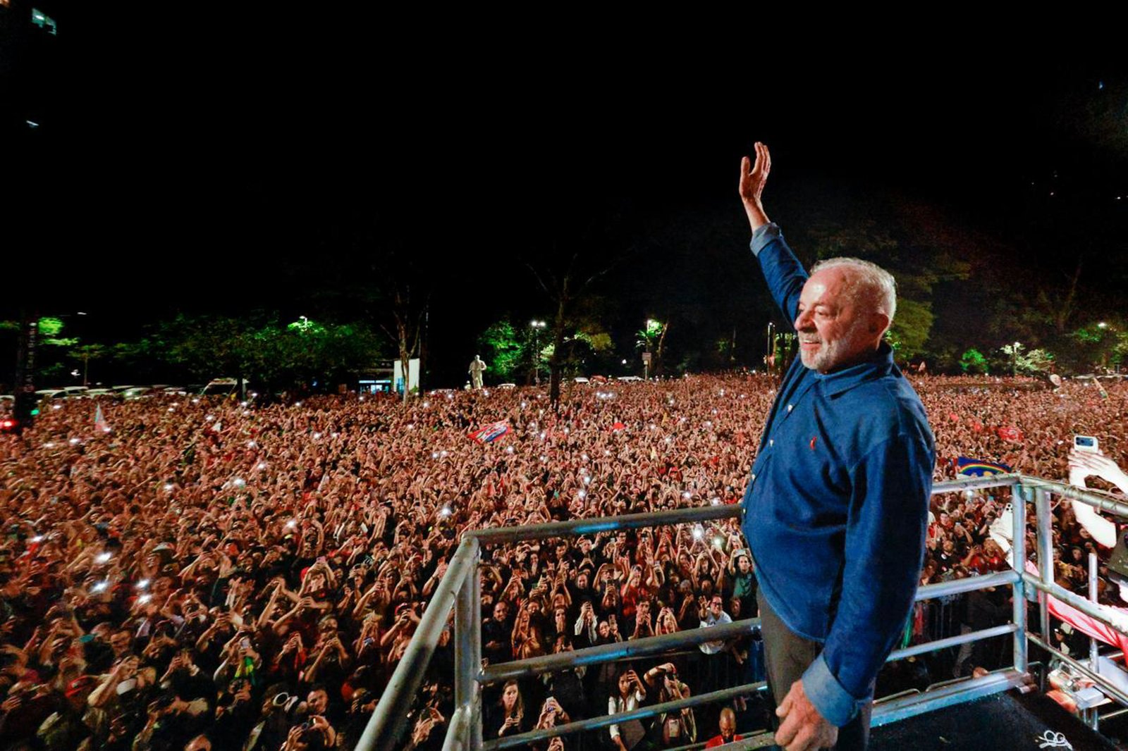 Presidente Luiz Inácio Lula da Silva acena para uma multidão de apoiadores durante evento político realizado à noite.
