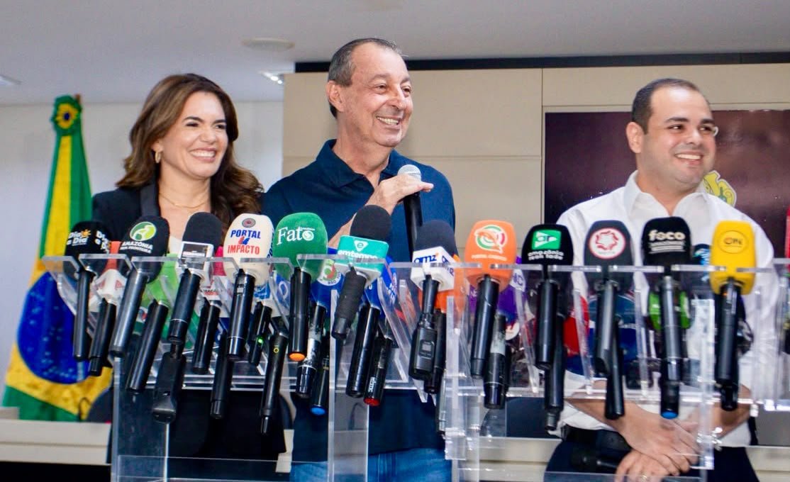 Omar Aziz aparece ao centro, segurando um microfone, ao lado de Alessandra Campêlo e Roberto Cidade durante coletiva de imprensa sobre a transição de governo no Amazonas.