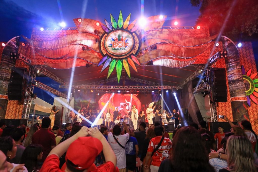 Palco iluminado do Boi Manaus com artistas se apresentando e público acompanhando o espetáculo