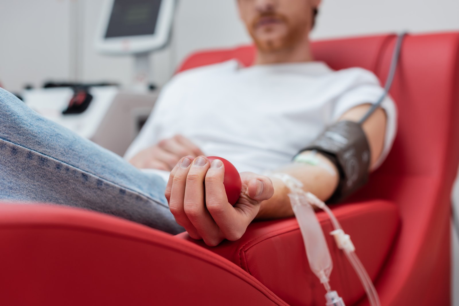 Homem realiza doação de sangue em uma cadeira de coleta, segurando uma bola vermelha para estimular a circulação durante o procedimento.